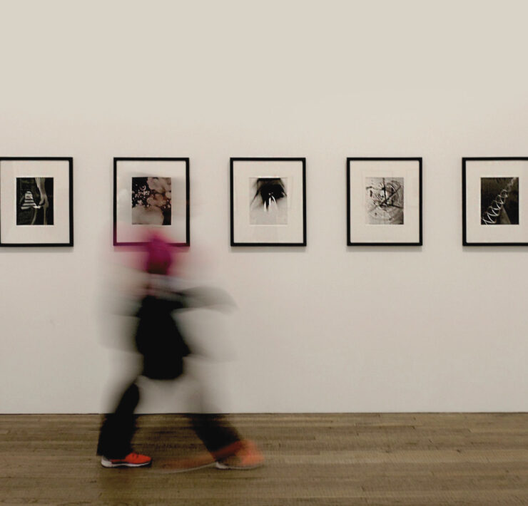 A minimalist gallery wall with five black-framed photos as a person walks past in motion blur.